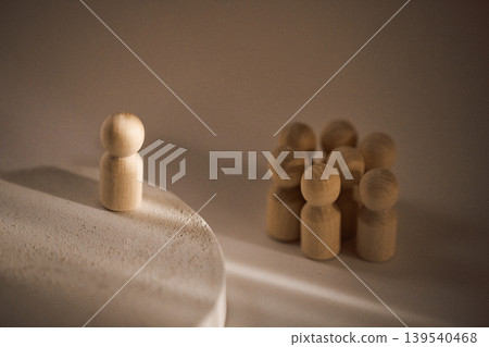Wooden figurine standing on a circular platform facing a group of smaller wooden figures arranged in a semi-circle on a neutral background Wooden figurine standing on a circular platform facing a group of smaller wooden figures arranged in a semi-circle on a neutral background 139540468
