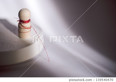 Wooden sewing mannequin with red thread wrapped around it, positioned on a circular base against a softly lit fabric background Wooden sewing mannequin with red thread wrapped around it, positioned on a circular base against a softly lit fabric background 139540470