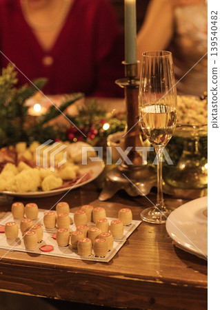Festive table setting with champagne glass, decorative candles, and assorted appetizers including bread and cheese on a wooden table during a holiday celebration 139540482