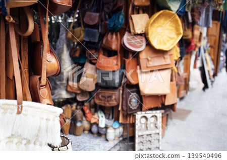 Leather bags and accessories displayed in a vibrant marketplace, showcasing craftsmanship and variety, with textures and colors creating an inviting shopping atmosphere Leather bags and accessories displayed in a vibrant marketplace, showcasing craftsmanship and variety, with textures and colors creating an inviting shopping atmosphere 139540496