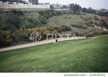 Scenic view of a couple in formal attire walking hand in hand on a grassy hillside, surrounded by lush greenery and a winding path, capturing a romantic outdoor moment Scenic view of a couple in formal attire walking hand in hand on a grassy hillside, surrounded by lush greenery and a winding path, capturing a romantic outdoor moment 139540502