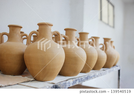 Row of handcrafted clay pottery vases displayed on a shelf in a bright studio, showcasing traditional craftsmanship and artistic design with natural textures Row of handcrafted clay pottery vases displayed on a shelf in a bright studio, showcasing traditional craftsmanship and artistic design with natural textures 139540519
