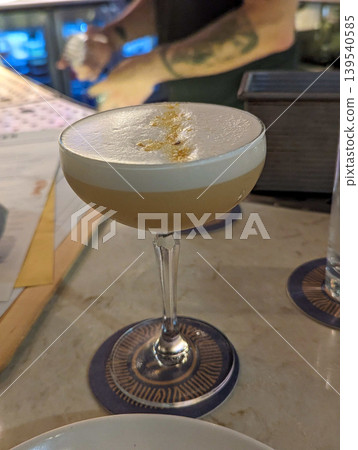 Elegant Craft Cocktail in Coupe Glass with Foam Top and Citrus Garnish in Modern Bar Setting 139540585
