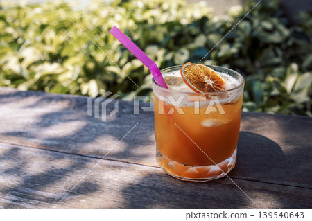 Close-up of a delicious citrus cocktail in a glass on a wooden round table Close-up of a delicious citrus cocktail in a glass on a wooden round table 139540643