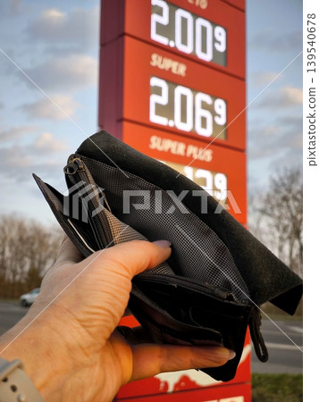 An empty black wallet in a hand against the backdrop of high fuel prices at a gas station 139540678