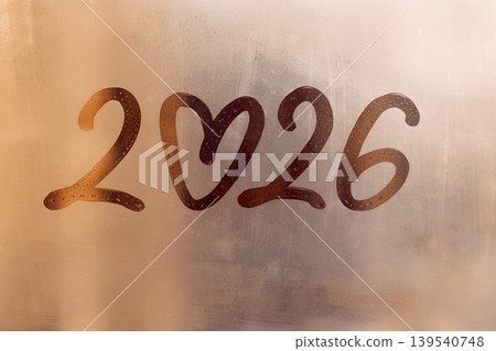 Handwritten arabic numerals 2026 with doodle heart shape on misted sunset glass on window flooded with raindrops 139540748