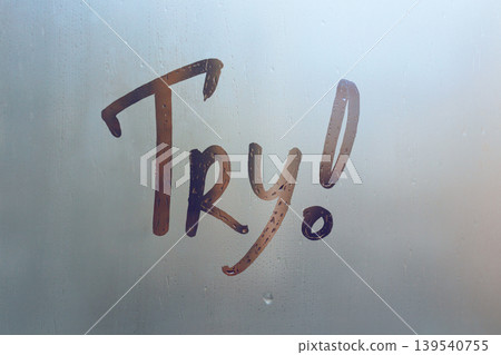 Handwritten lettering Try and exclamation mark on misted glass sunset window with raindrops, concept of full life and motivation Handwritten lettering Try and exclamation mark on misted glass sunset window with raindrops, concept of full life and motivation 139540755