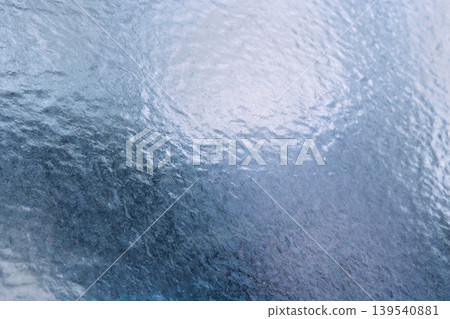 Textured blue glass surface with rippled patterns reflecting light, creating an abstract background suitable for design and artistic applications Textured blue glass surface with rippled patterns reflecting light, creating an abstract background suitable for design and artistic applications 139540881