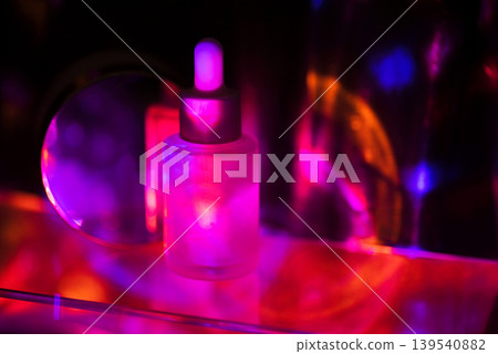 Glass dropper bottle with a silver cap illuminated by colorful lights, creating a vibrant display of pink, purple, and blue reflections on a reflective surface 139540882