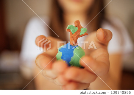 Child holding a small globe made of clay with a tree on top, showcasing a creative representation of Earth and nature in a close-up view 139540896