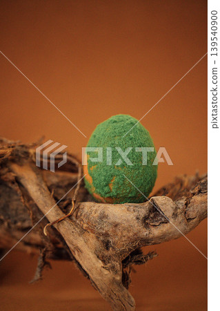 Green felted egg placed on a textured wooden branch against a warm brown background, showcasing a unique decorative element for seasonal displays or crafts Green felted egg placed on a textured wooden branch against a warm brown background, showcasing a unique decorative element for seasonal displays or crafts 139540900