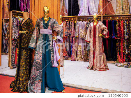 Elegant traditional dresses displayed on mannequins in a boutique, showcasing intricate designs and vibrant colors in a well-organized clothing store interior Elegant traditional dresses displayed on mannequins in a boutique, showcasing intricate designs and vibrant colors in a well-organized clothing store interior 139540903