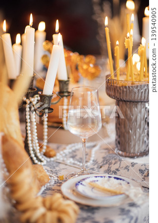 Elegant dining table set for a festive occasion with lit candles, glass of water, decorative bread, and intricate tableware arranged for a special gathering 139540905