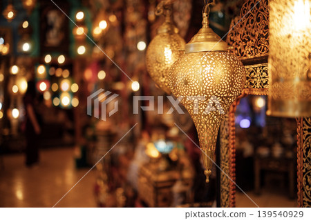 Ornate golden lanterns hang in a vibrant marketplace, casting warm light and intricate shadows, creating an enchanting atmosphere filled with cultural richness and artistic craftsmanship 139540929
