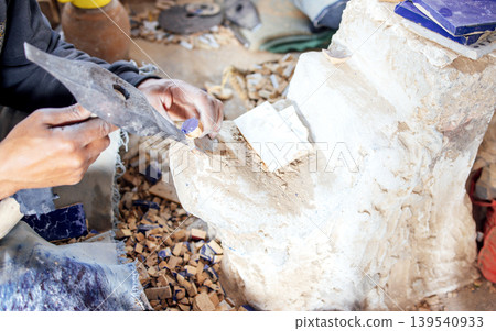 Skilled artisan shaping stone with hand tools, surrounded by fragments and dust, showcasing craftsmanship and dedication in a creative workspace environment Skilled artisan shaping stone with hand tools, surrounded by fragments and dust, showcasing craftsmanship and dedication in a creative workspace environment 139540933