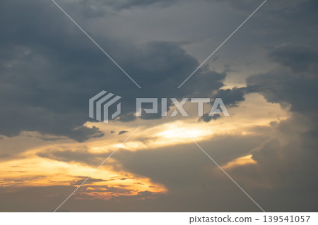 Dark clouds drift across a glowing evening sky as warm sunlight breaks through, creating a dramatic contrast of light and shadow, ideal for atmospheric backgrounds and nature concepts. Dark clouds drift across a glowing evening sky as warm sunlight breaks through, creating a dramatic contrast of light and shadow, ideal for atmospheric backgrounds and nature concepts. 139541057