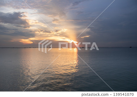 Delicate evening colors blend across the sky as the sun dips low, casting a smooth reflective trail over gentle water. Minimal coastal elements enhance the tranquil and airy mood. Delicate evening colors blend across the sky as the sun dips low, casting a smooth reflective trail over gentle water. Minimal coastal elements enhance the tranquil and airy mood. 139541070