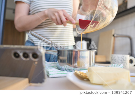 Woman pours batter from glass bowl into saucepan with whisk Woman pours batter from glass bowl into saucepan with whisk 139541267