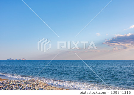 Pebble beach with blue sea under scattered clouds Pebble beach with blue sea under scattered clouds 139541316