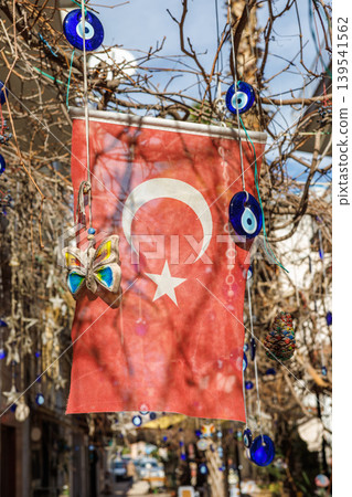 Turkish flag hanging with blue nazar charms on a tree branch Turkish flag hanging with blue nazar charms on a tree branch 139541562