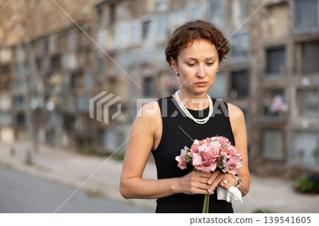 Sorrowful woman in black standing in cemetery with flowers Sorrowful woman in black standing in cemetery with flowers 139541605