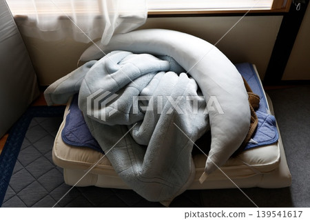 A morning spent haphazardly tidying up futons and pillows in a dimly lit room. Bedding piled up on the bed. A morning spent haphazardly tidying up futons and pillows in a dimly lit room. Bedding piled up on the bed. 139541617