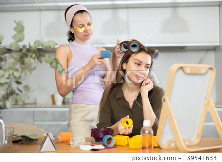 Adult woman curls hair of young woman Adult woman curls hair of young woman 139541633