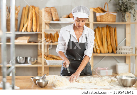 Female baker cutting raw dough with knife to make croissants or buns 139541641