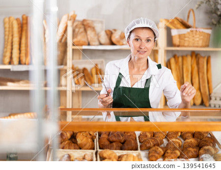 Female baker holds basket with finished products, shows different croissants. Female baker holds basket with finished products, shows different croissants. 139541645