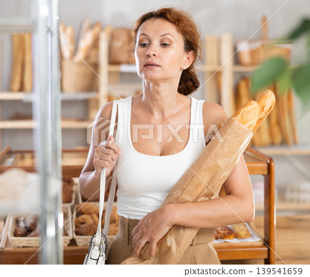 Female shopper with bag of fresh bread and baguettes in bakery Female shopper with bag of fresh bread and baguettes in bakery 139541659