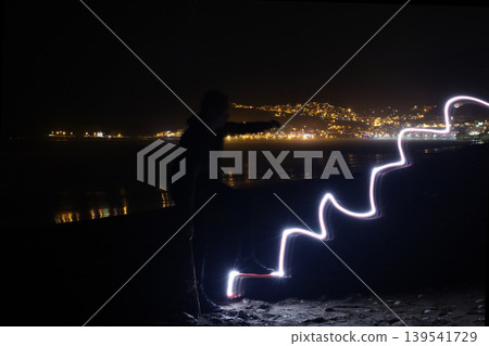 Silhouette of man climbing glowing light painting stairs on beach at night 139541729