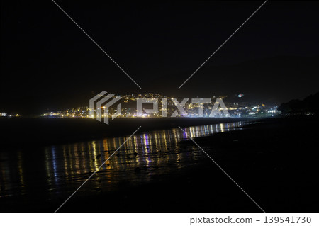Night landscape of illuminated coastal town lights reflecting on wet sand 139541730