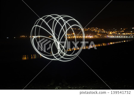 Abstract white light painting sphere on night beach with city background 139541732