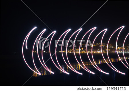 Abstract light painting trails over coastal city night skyline Abstract light painting trails over coastal city night skyline 139541733