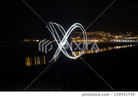 Abstract light painting trail on dark beach at night with city lights background 139541734