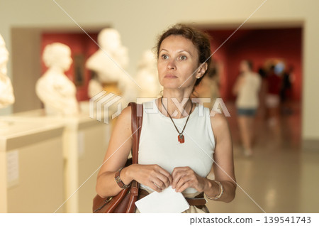 Woman looks at museum sculptures with brochure Woman looks at museum sculptures with brochure 139541743