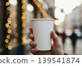 Hand holding a steaming paper cup with blurred bokeh lights 139541874