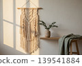Macrame wall hanging, eucalyptus in vase on shelf, and green linen throw on stool in warm sunlight 139541884