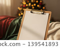 A blank clipboard with paper next to a christmas tree 139541893