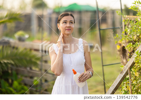 Adult woman applying repellent in cottage garden Adult woman applying repellent in cottage garden 139542776