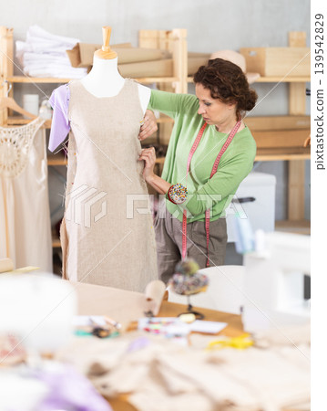 Woman tailor connects parts of dress on mannequin 139542829