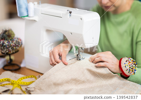 Hands of seamstress sewing linen fabric on machine Hands of seamstress sewing linen fabric on machine 139542837
