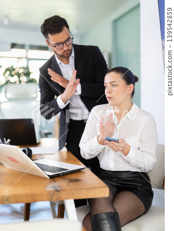 Businessman complains to subordinate about her talking on her mobile phone while working in office Businessman complains to subordinate about her talking on her mobile phone while working in office 139542859