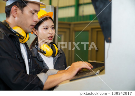 Industrial engineers operating machine control panel in factory environment Industrial engineers operating machine control panel in factory environment 139542917