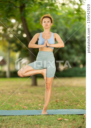 Adult woman doing yoga in tree pose Adult woman doing yoga in tree pose 139542929