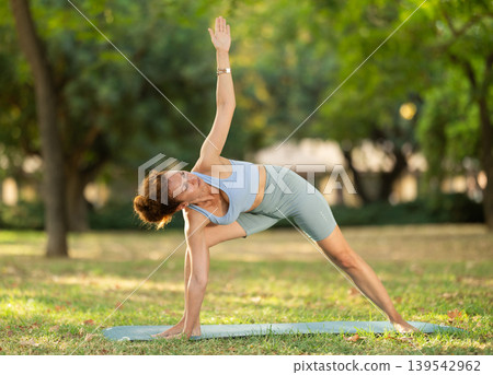 Woman practicing yoga in garden, performing Anjaneyasana, or Crescent Moon Pose Woman practicing yoga in garden, performing Anjaneyasana, or Crescent Moon Pose 139542962