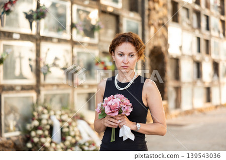 Woman in black mourning dress standing with flowers near columbarium 139543036