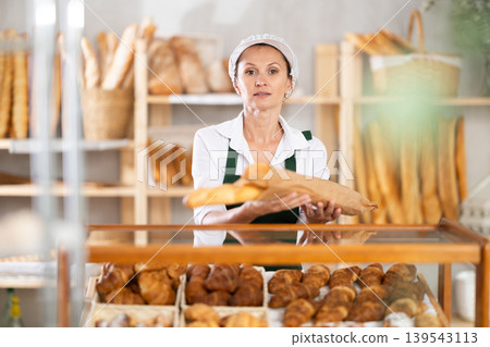 Woman seller took fresh loaves of white flour out of window in bakery Woman seller took fresh loaves of white flour out of window in bakery 139543113