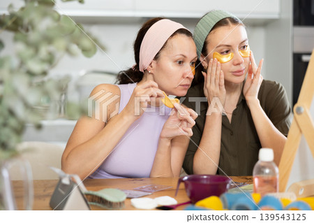 Two besties applying golden under-eye patches in home setting Two besties applying golden under-eye patches in home setting 139543125
