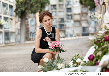 Grieving woman in black placing bouquet on grave Grieving woman in black placing bouquet on grave 139543159